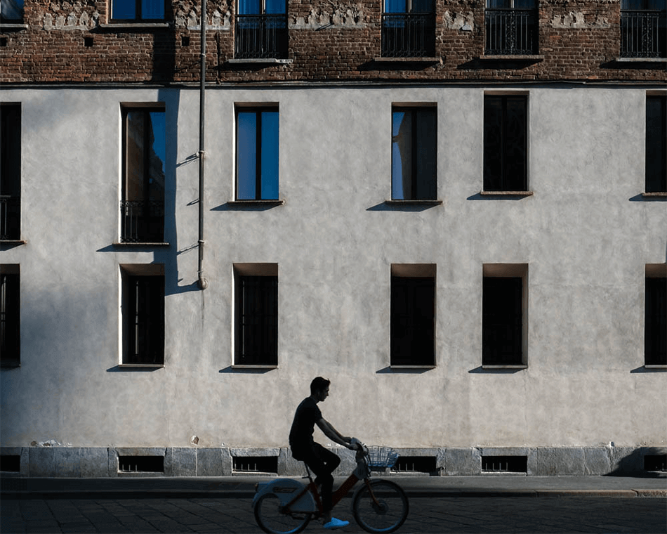旅行幾何系列攝影作品,拍攝地點為義大利街頭拍攝,男子騎腳踏車經過建築物前,構圖為排列整齊的窗戶