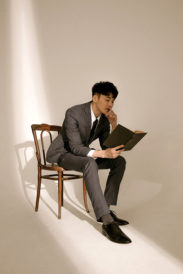 牛津鞋 坐在木椅上閱讀的模特穿著深灰色西裝搭配林果良品的1/4雕花橫飾經典黑色牛津鞋