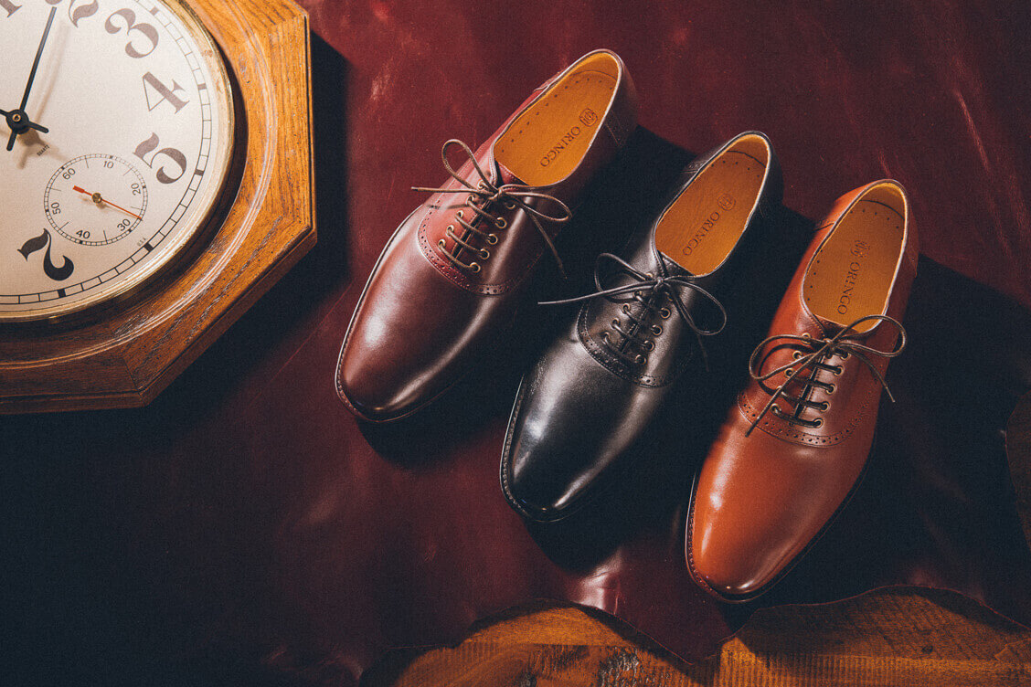 黑色咖啡色和雙配色周年款鞍部牛津鞋與時鐘一同放在皮革上