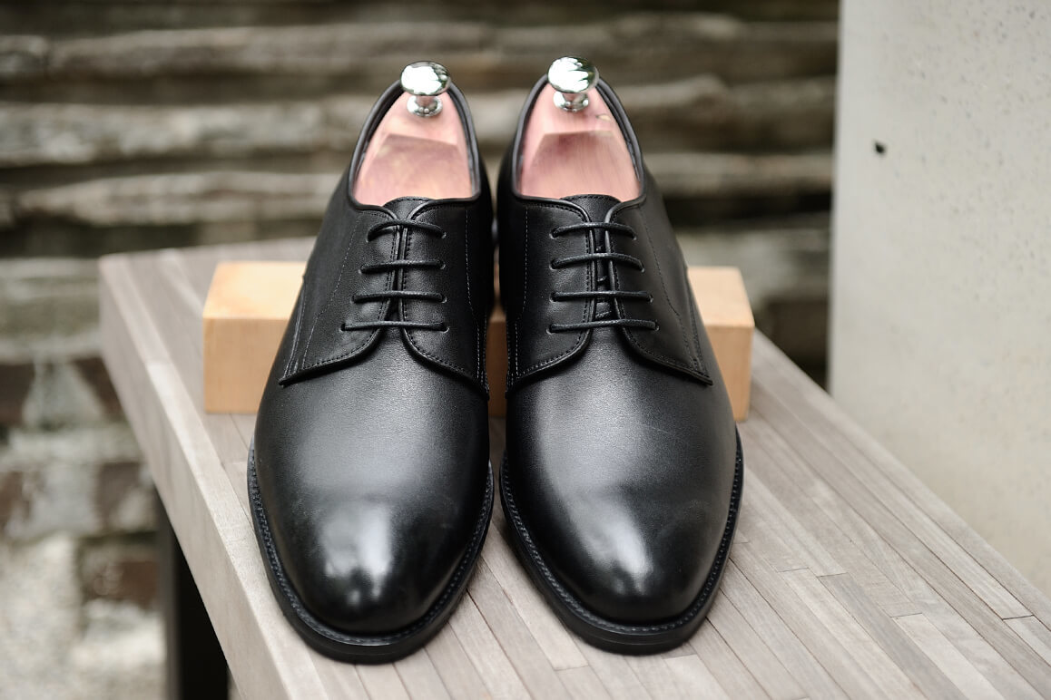 戶外的長木板凳上擺著一雙放有原木斜撐的黑色德比鞋