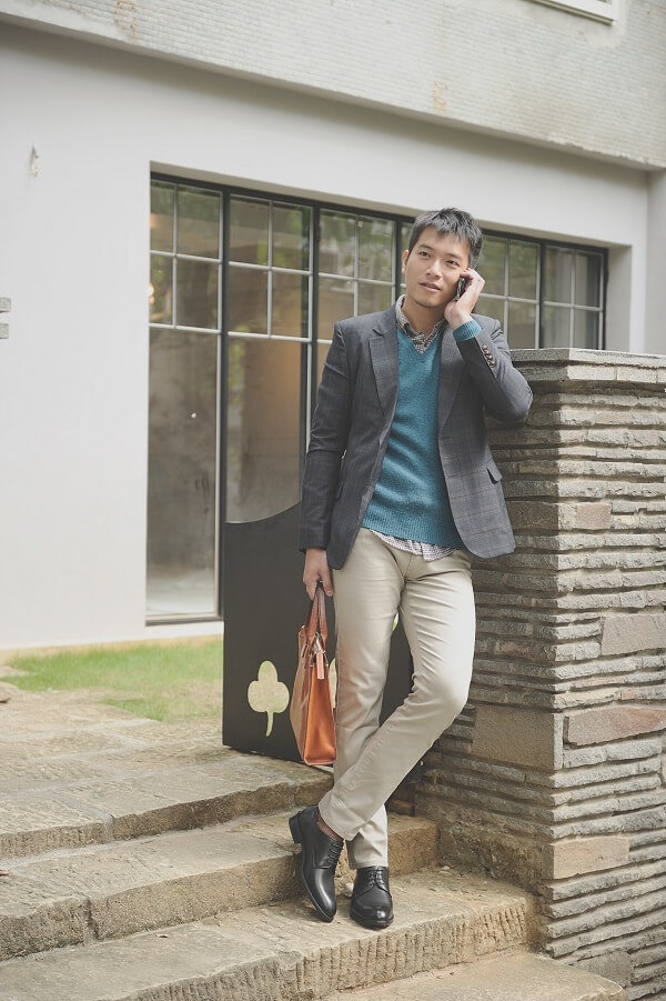 身穿灰色西裝外套搭配卡其褲與黑色德比鞋的模特兒接聽手機
