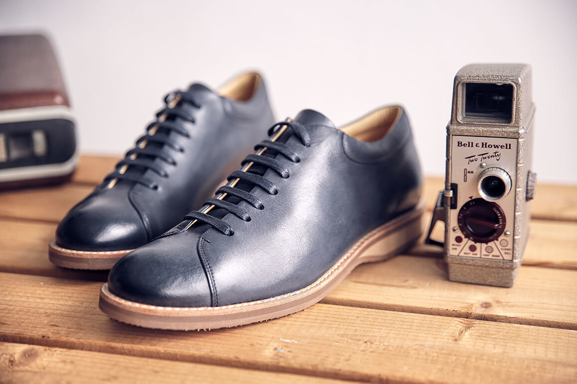 橫條木椅上放著一雙闇夜藍色皮革休閒鞋與一台舊式相機