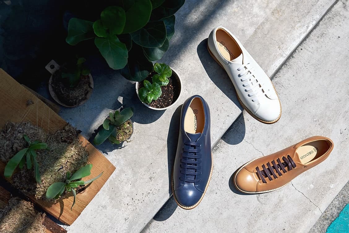 皮革休閒鞋 俯視三只皮革休閒鞋白色闇夜藍色焦咖啡色與小盆栽沐浴灑滿陽光的台階上