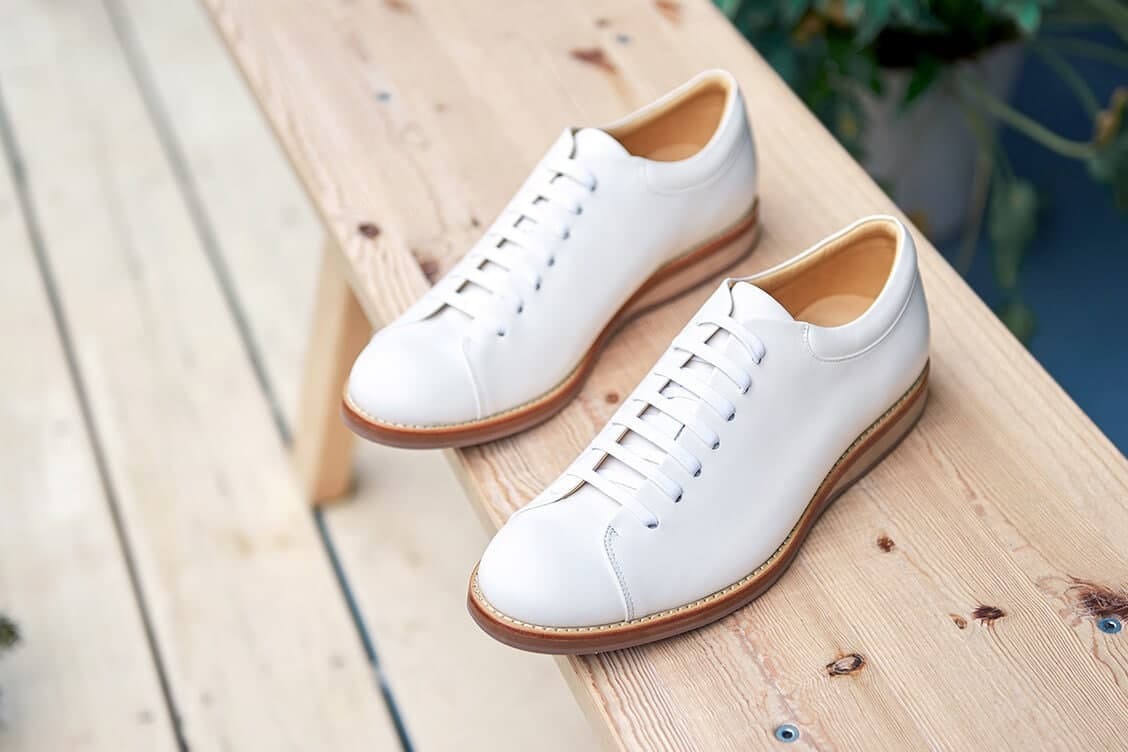 皮革休閒鞋 一雙白色的皮革休閒鞋鞋側擺放在原色木椅上