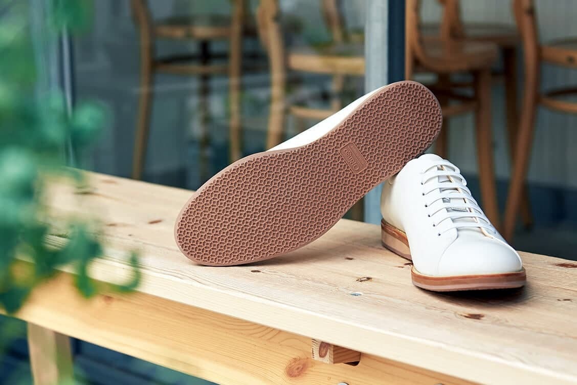皮革休閒鞋 窗台前的木椅上一雙白色的皮革休閒鞋一正一反的展示裸棕色的鞋底