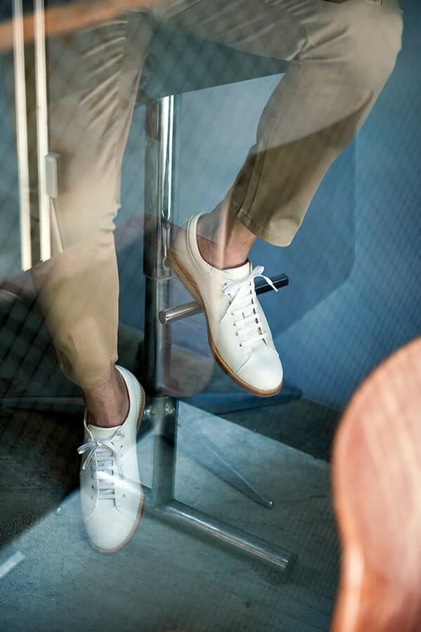 皮革休閒鞋 腳步特寫穿著卡其褲搭配白色皮革休閒鞋的模特坐在窗邊的高腳椅上