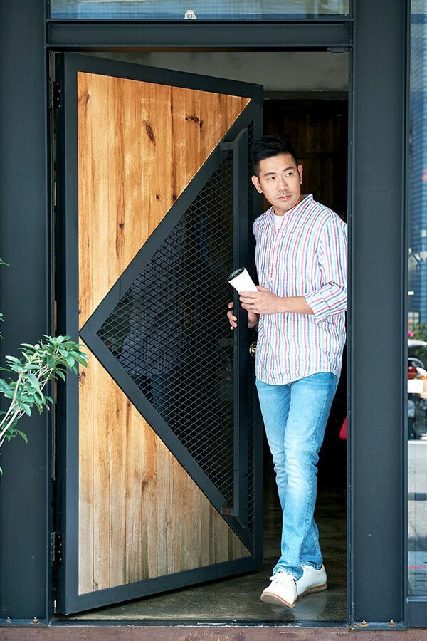 皮革休閒鞋 穿著條紋休閒襯衫與牛仔褲搭配白色皮革休閒鞋的模特開門望向左方走出咖發廳