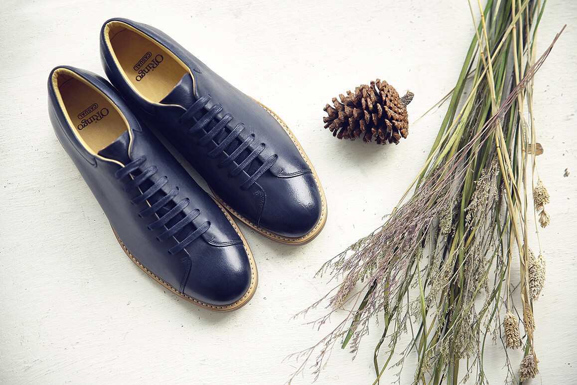 一雙闇夜藍色皮革休閒鞋與一束薰衣草和一粒松果擺在白色檯面上