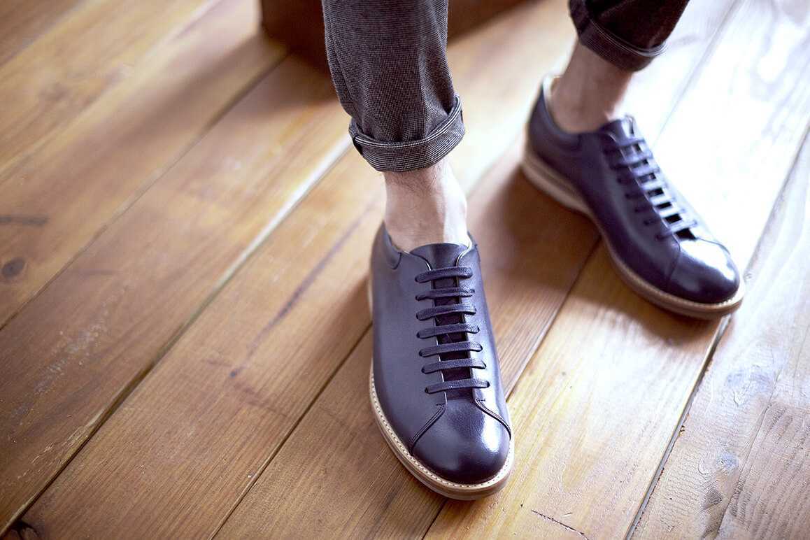 腳部特寫穿著闇夜藍色皮革休閒鞋搭配兔灰色休閒西裝褲的模特兒站在木質地板上