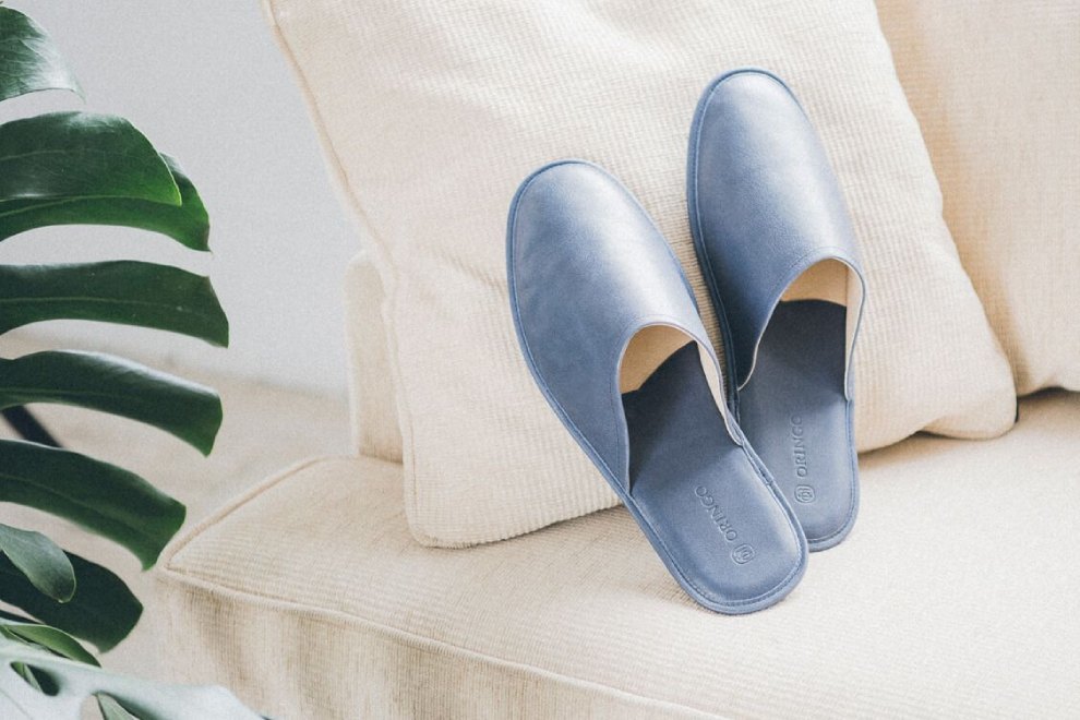 牛皮室內拖鞋 一雙湛藍色牛皮室內拖鞋倚靠在米白色沙發的抱枕上