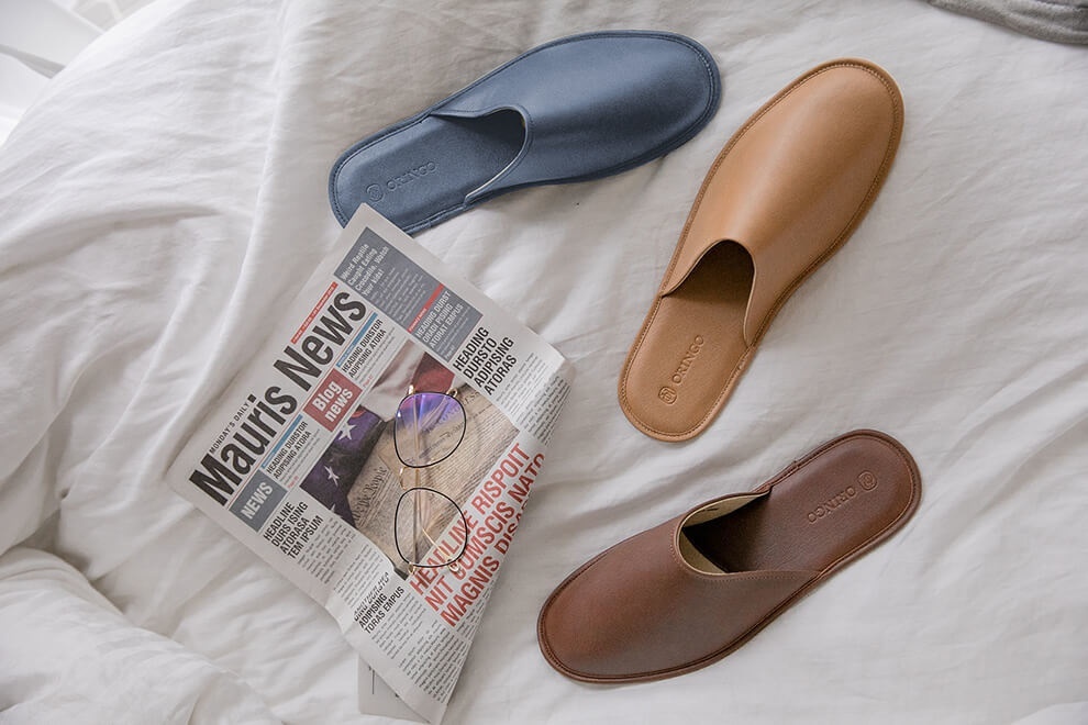 白色被單上擺著湛藍色、可可棕和奶茶棕牛皮拖鞋及眼鏡和一份英文報紙