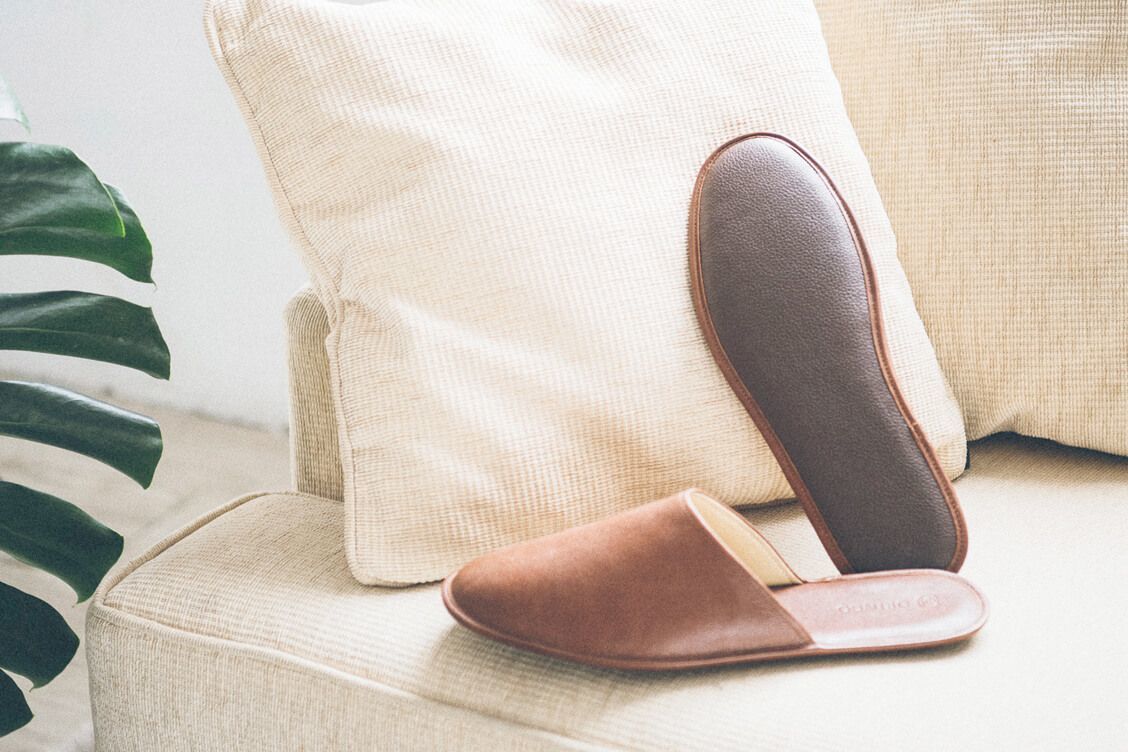 一正一反的可可棕色牛皮室內拖鞋放在米白沙發上