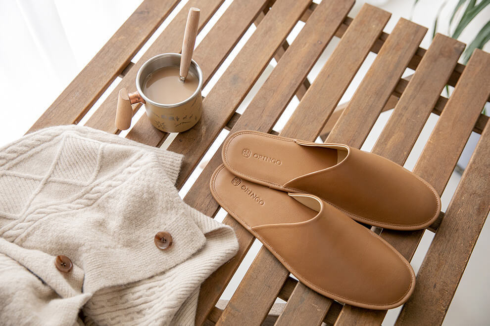 摺疊木桌上有一杯咖啡和米白毛衣與一雙奶茶棕色的牛皮室內拖鞋