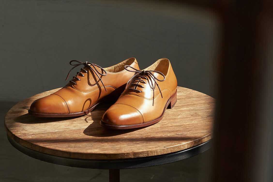 木質小圓桌上擺著一雙蜜糖棕色的鵝頸橫飾皮底牛津鞋