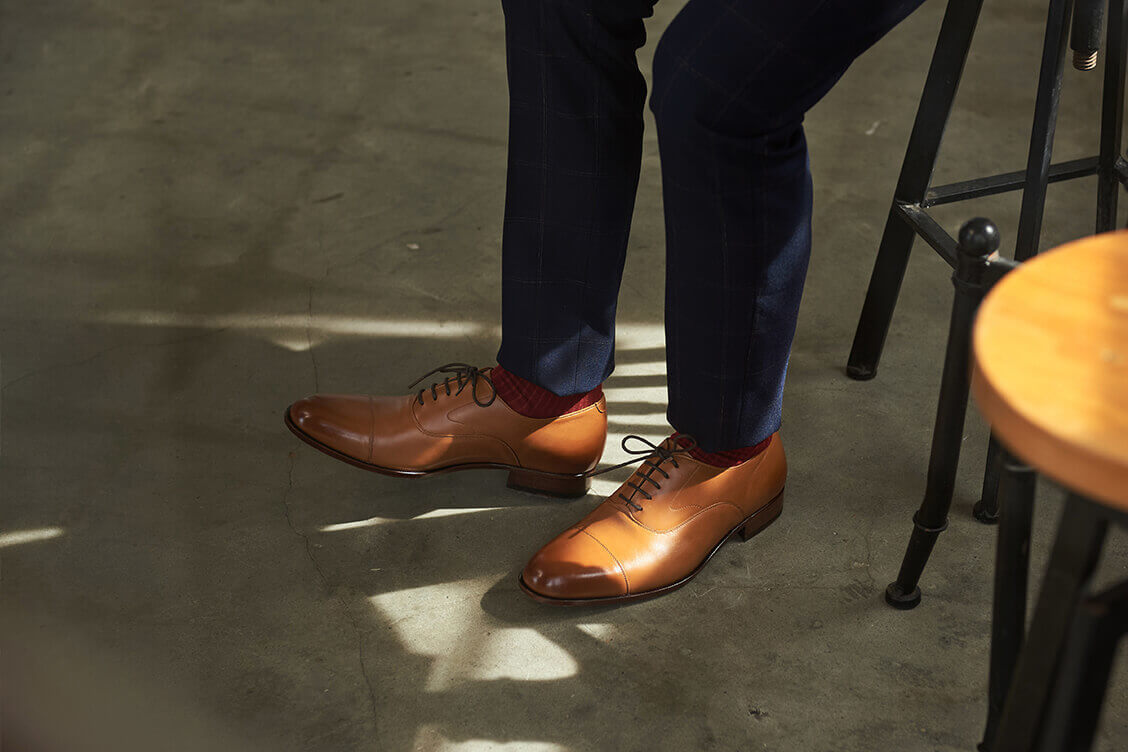 特寫模特展示深藍商務西裝搭配蜜糖棕色的牛津鞋