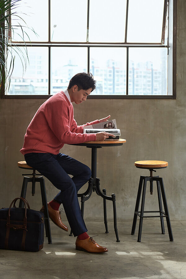 穿著粉紅毛衫與藍色西褲的模特搭配蜜糖棕色的牛津鞋