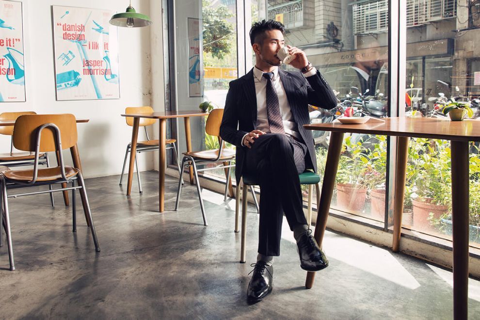 牛津鞋 穿著正式黑色西裝搭配黑色牛津鞋的模特坐在窗邊品嘗咖啡