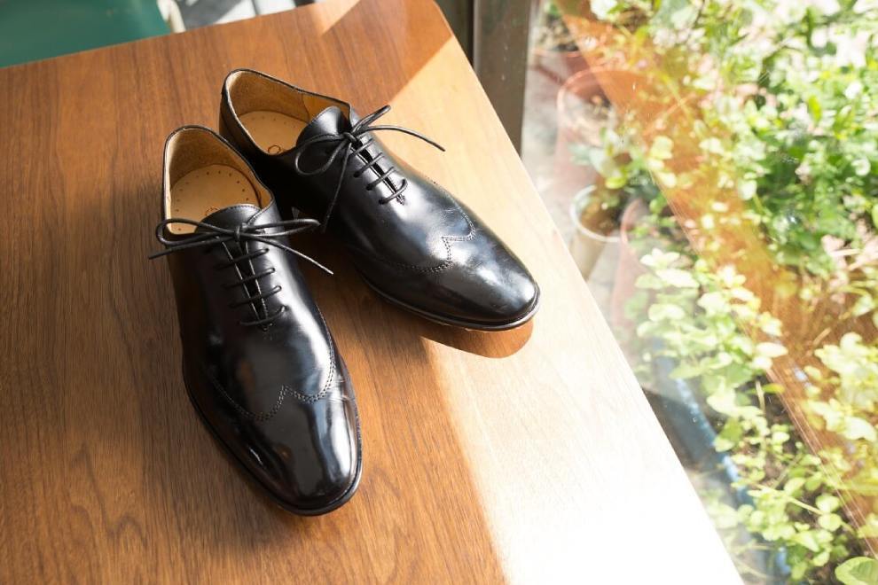 牛津鞋 一雙黑色翼紋縫線牛津鞋展示於窗檯邊的木桌上