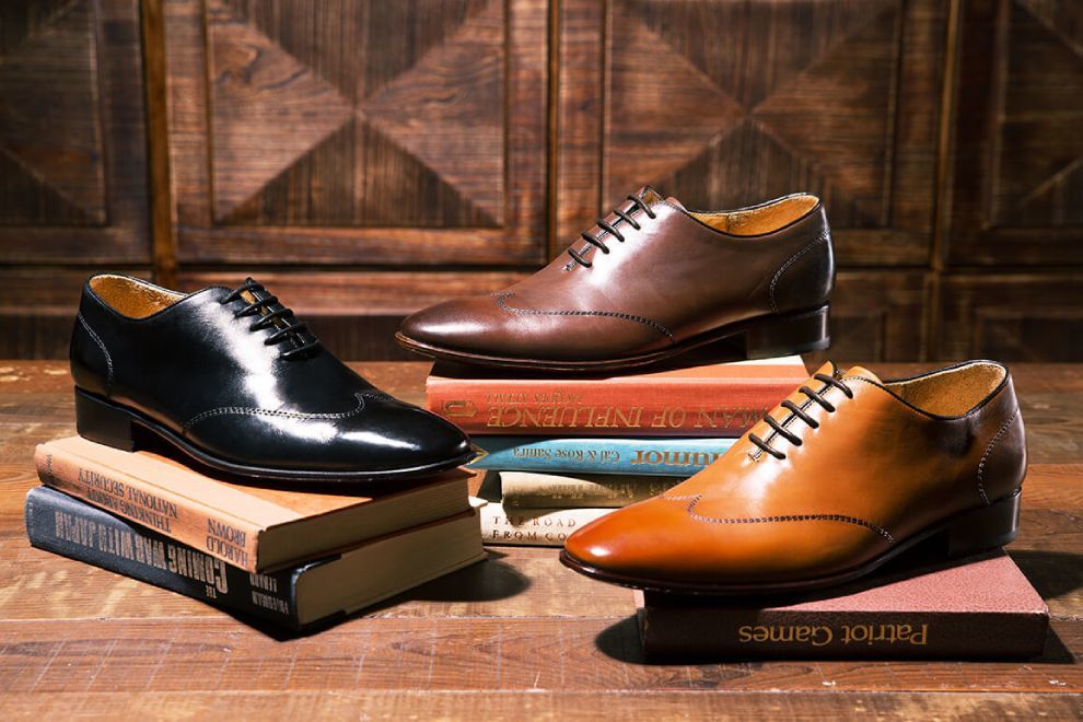 單只黑色蜜棕色咖啡色翼紋縫線皮底牛津鞋交錯墊著書疊放在木紋地板上