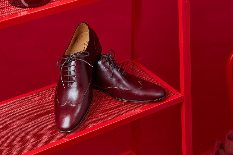 一雙酒紅色的油感皮料的牛津鞋擺放在紅色鐵製書架上