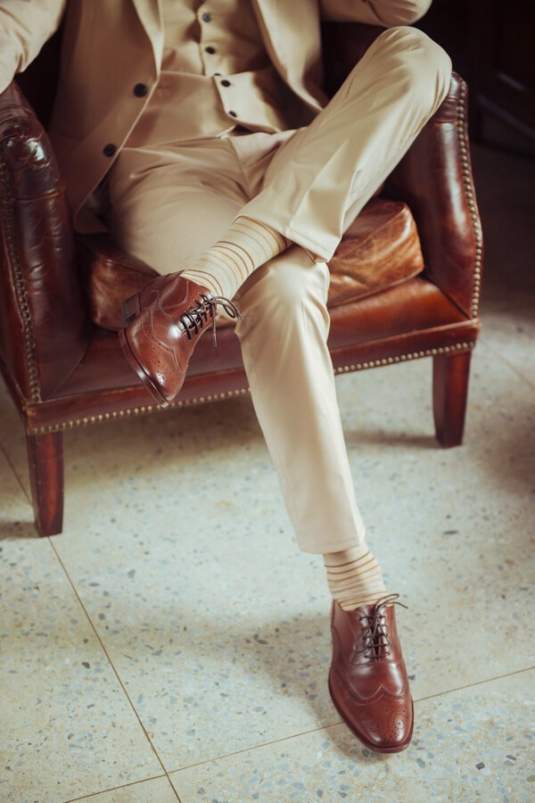 牛津鞋 坐姿模特展示可可咖色3/4雕花鋸齒翼紋牛津鞋搭配米色西裝褲