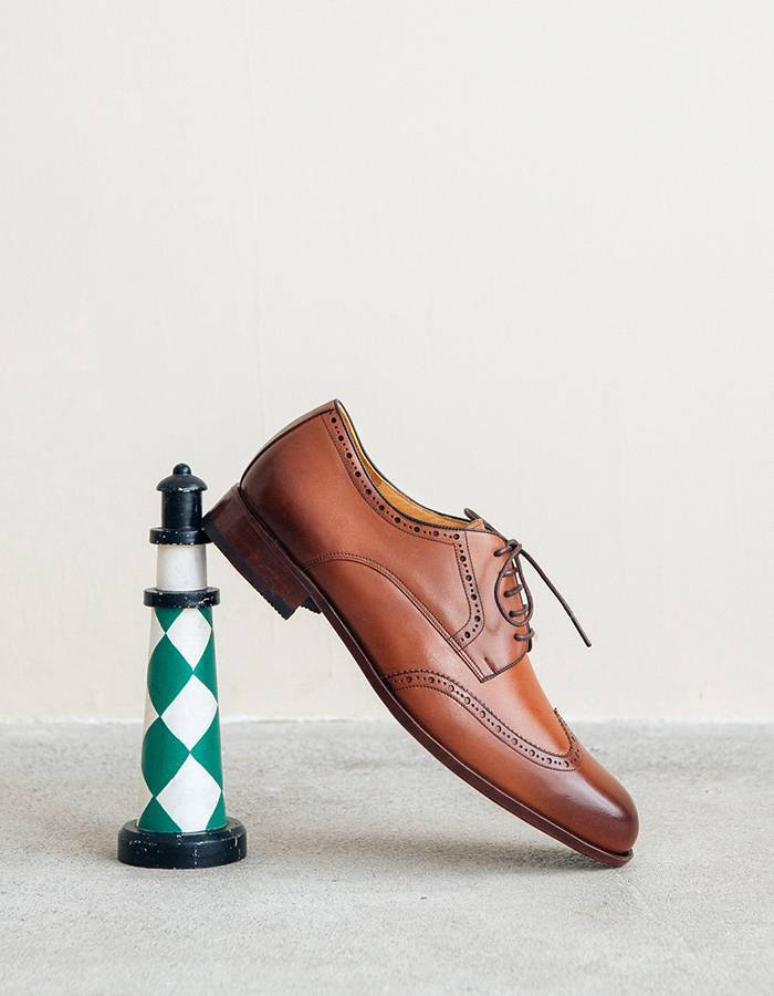 德比鞋 展示斜架在燈塔擺飾的焦糖棕色的翼紋雕花德比鞋斜身側面
