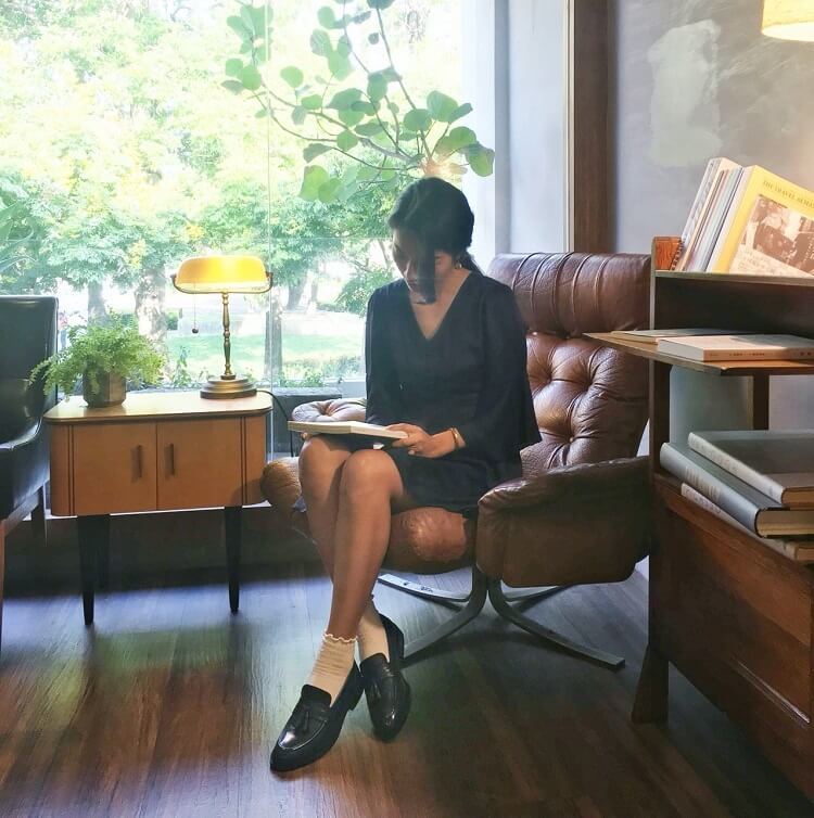 一名女人穿著黑色洋與黑色流蘇樂福鞋低頭看書
