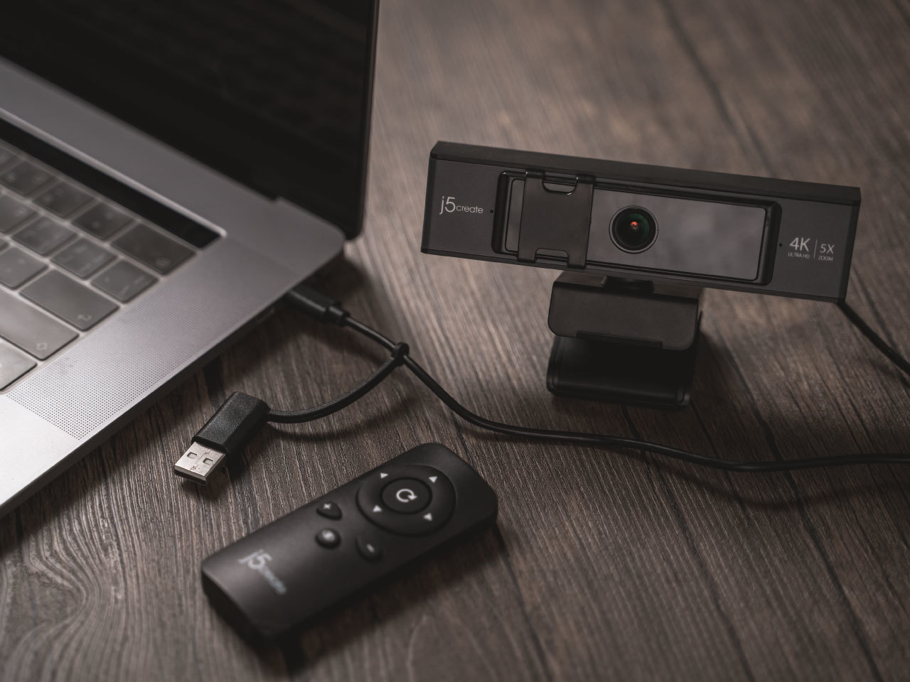 右邊有一台黑色視訊攝影機，左邊有一台Apple的筆電和視訊攝影機的遙控器。