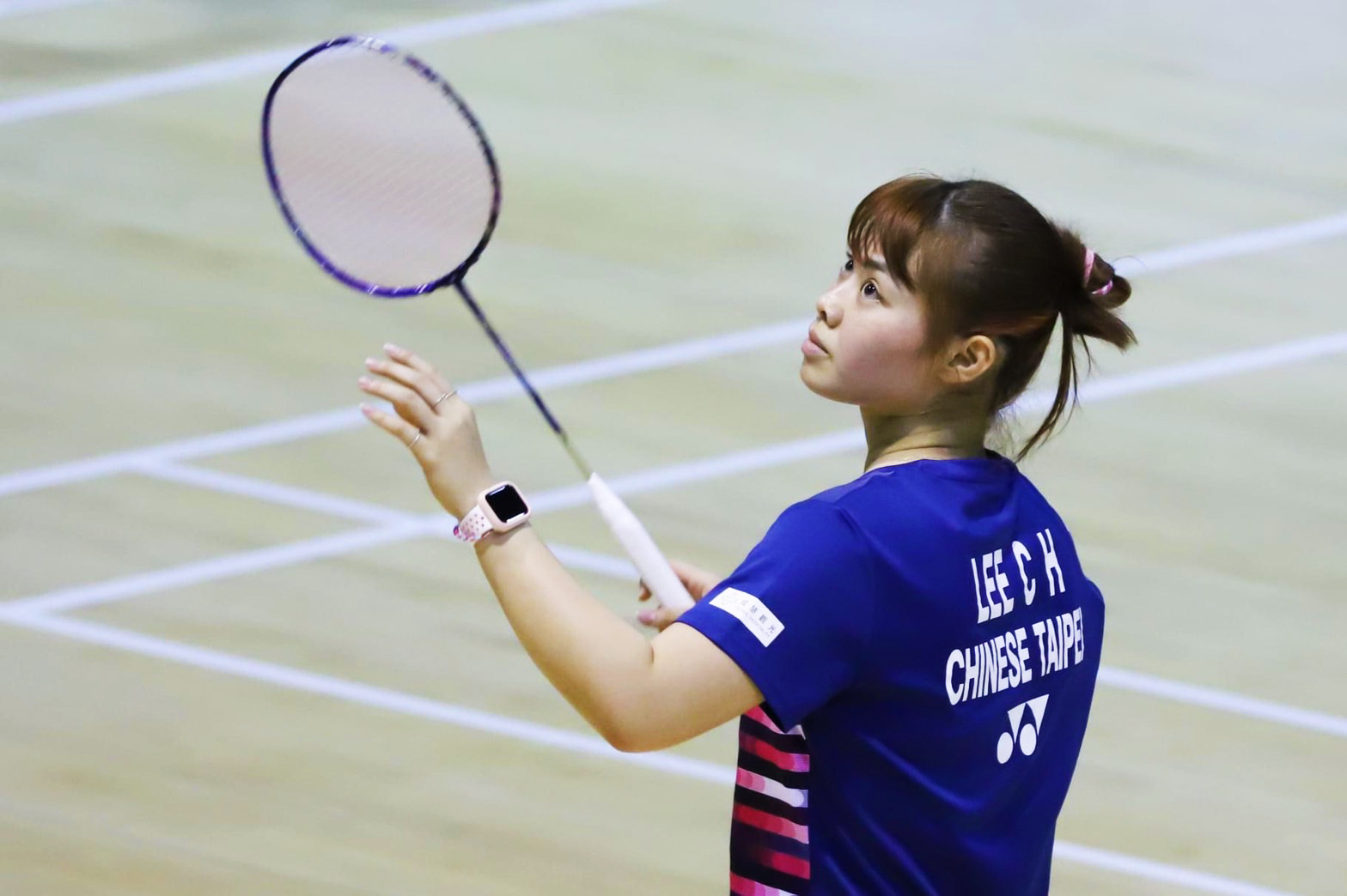 羽球選手李佳馨在羽球場上，身穿藍色衣服，右手拿著球拍，眼睛盯著左上方準備出擊。