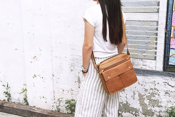 揹著真皮側背包經過斑駁的牆