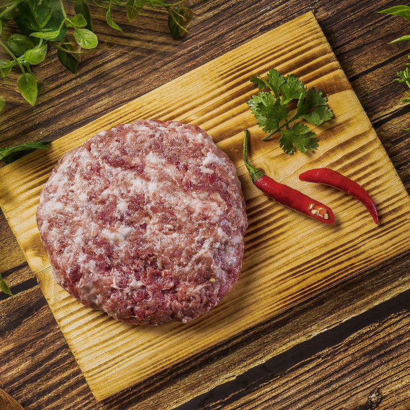 木砧板上壓成圓餅狀的山野豚絞肉,旁邊放著紅辣椒