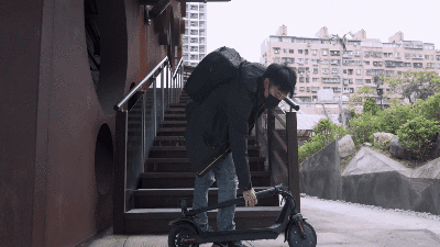 有一位男生提著折疊的Wayax X7電動滑板車上樓梯