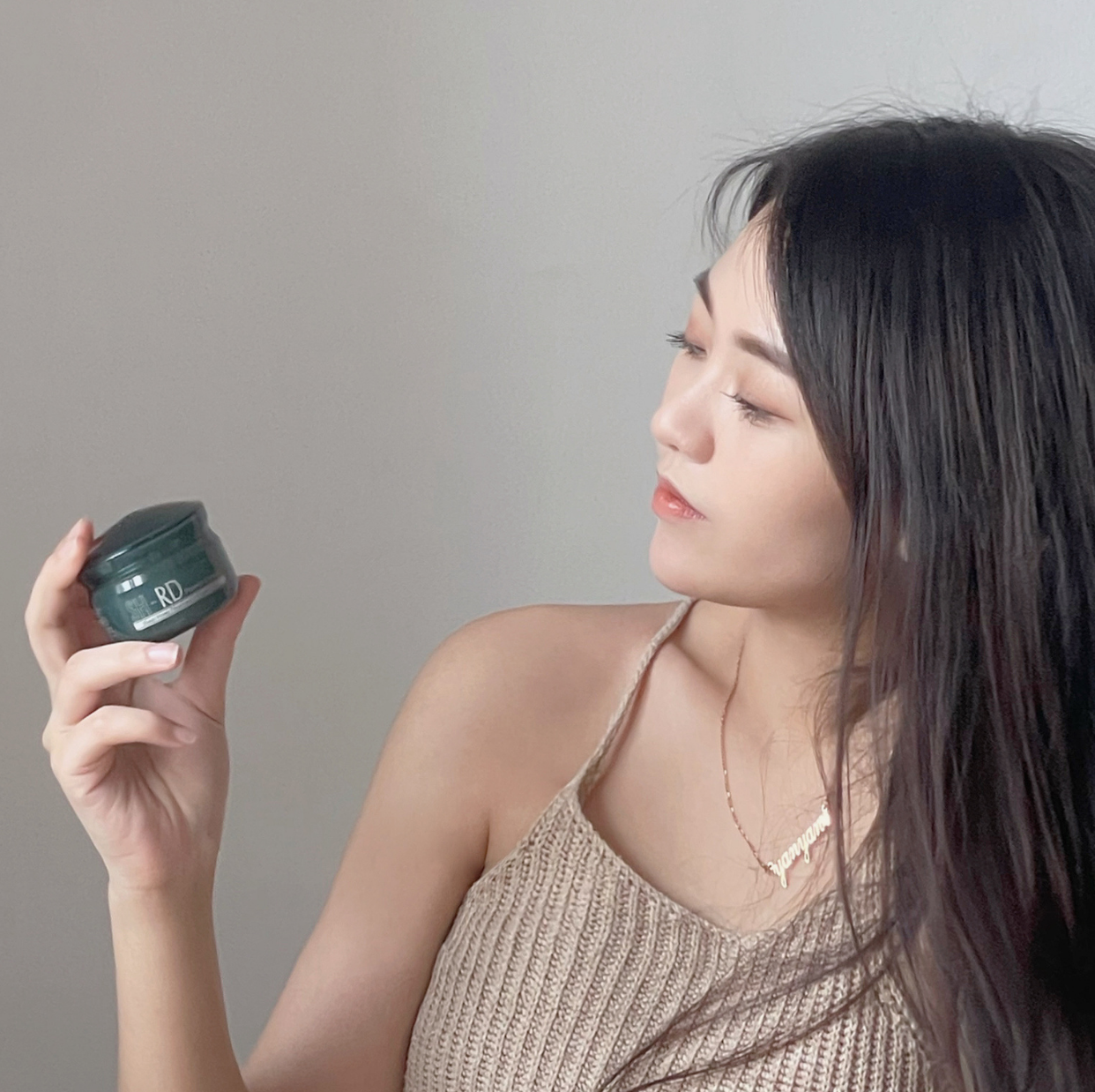 一位马来西亚长发网红看着手中的SH-RD绿色瓶身的蛋白质护发霜。
