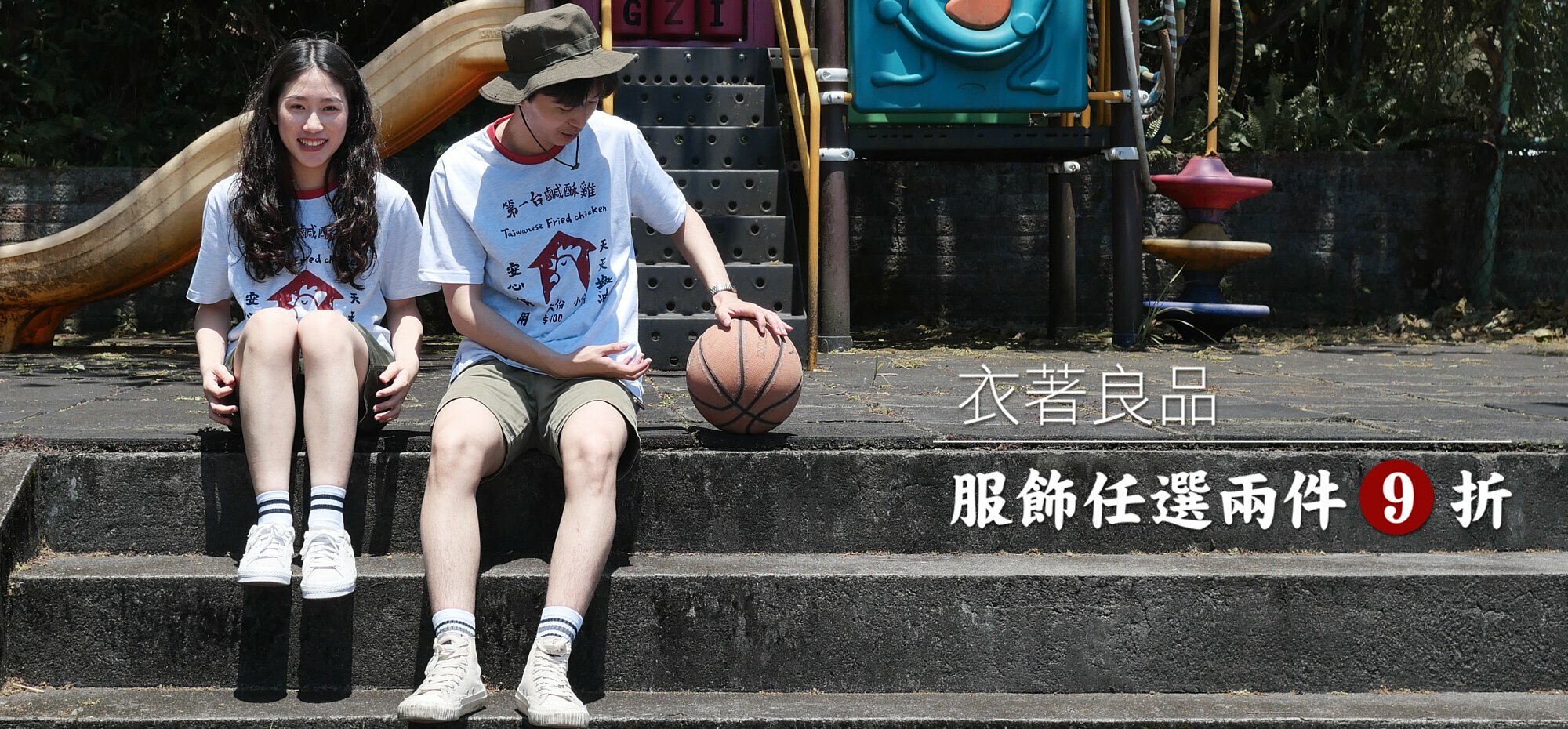 上頭有文字：衣著良品任選2件9折 。背景是公園的兒童遊具，一男一女坐在水泥階梯上，身穿鹹酥雞招牌印花T恤，看起來很開心。