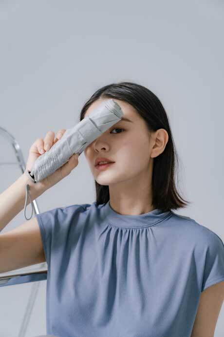 一位女性，右手拿一把白色的OMBRA P1Air 極輕防曬傘，遮住右眼很時尚的感覺