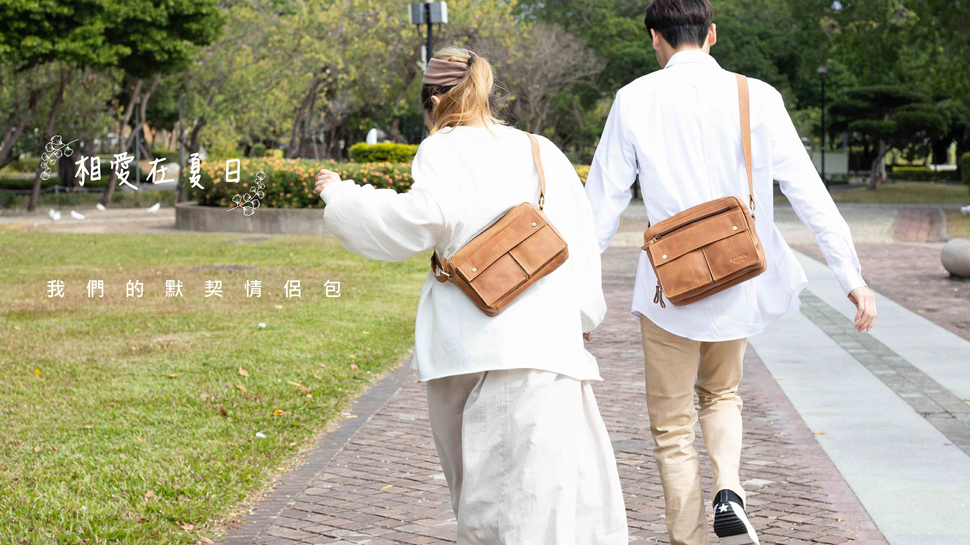 一女一男斜揹著駝色後背包 手牽手在公園奔跑