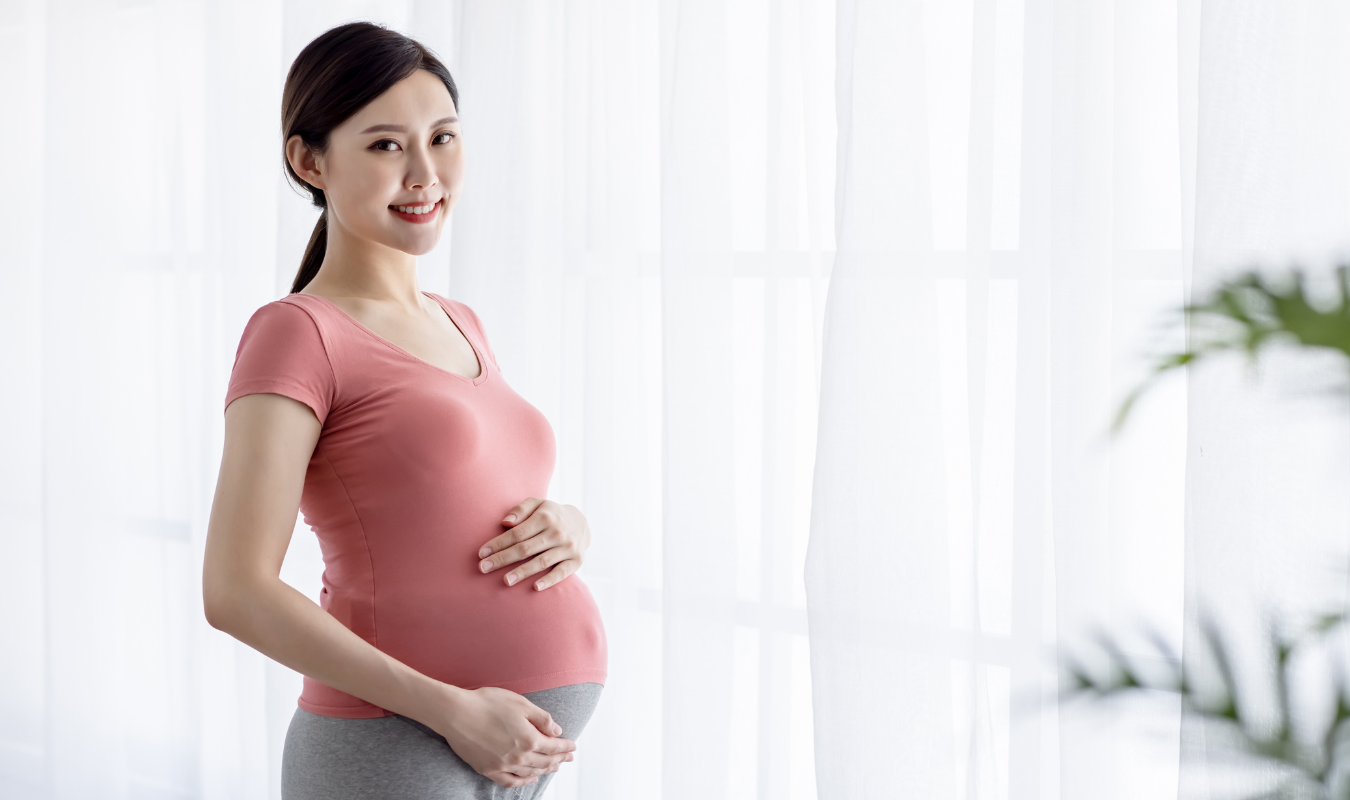 一個擁有好心情的孕婦，微笑的輕捧著孕肚｜逗DOLL SPA孕婦按摩