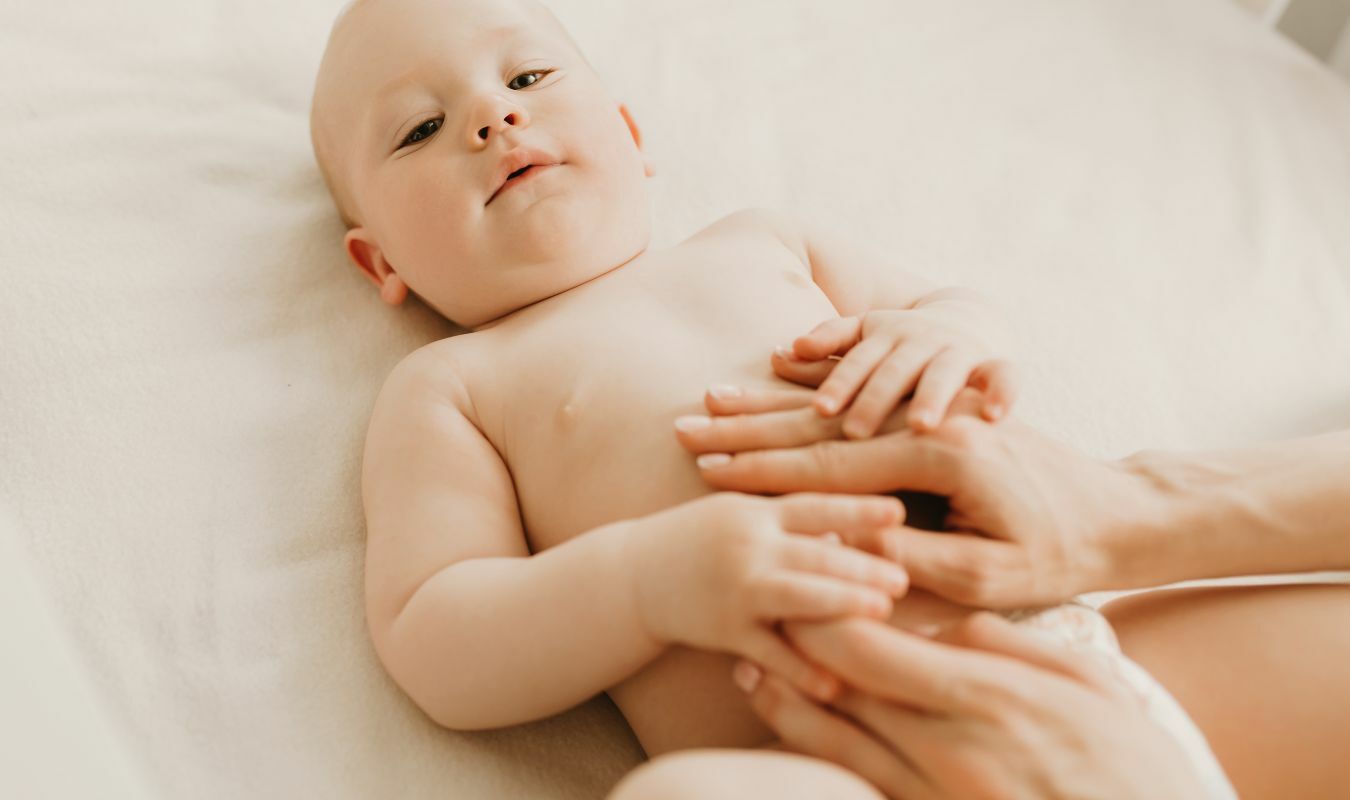 寶寶雙腳抬起，手貼在寶寶腹部進行按摩的畫面｜逗DOLL SPA好孕寶寶純淨按摩油