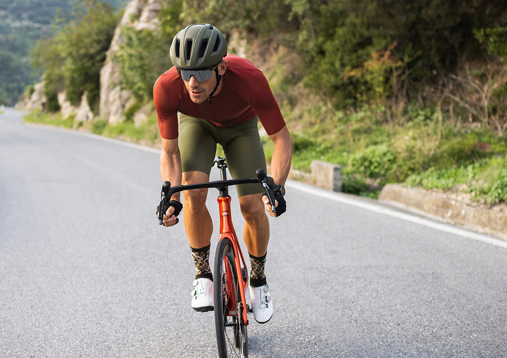 專業自行車選手在山上騎公路車身穿紅色PIUMA系列極輕量級專業自行車衣加卡其綠CODE系列專業自行車褲,頭上戴著自行車安全帽和戴著運動眼鏡賣力踩踏