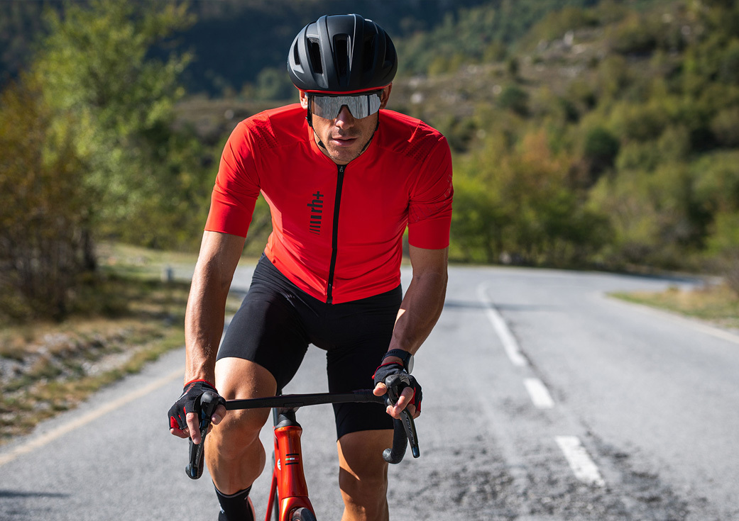 專業自行車手騎著公路車穿紅色素面競賽級自行車衣加黑色XTRM系列競賽級自行車褲,手上戴自行車手套正在爬坡