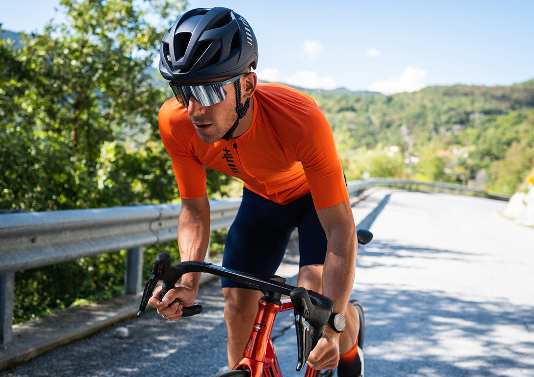 專業自行車選手穿著橘色素面輕量級專業自行車衣搭配深藍色素面專業級吊帶自行車褲騎著公路車在爬坡