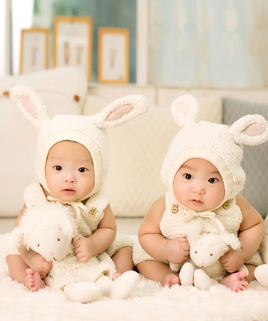 兩個戴著兔子帽的亞洲嬰兒正在玩泰迪熊。