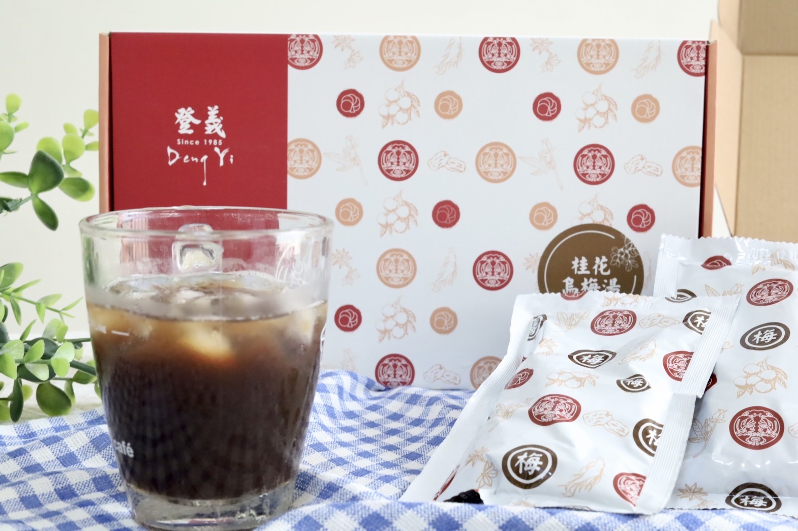 一杯清涼消暑的桂花烏梅湯、兩包桂烏擺放在一旁、一盒桂花烏梅湯濃縮包在後面