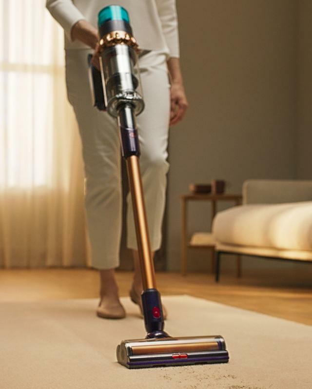 一位女士正在使用Dyson 吸塵器對客廳的地毯進行吸塵