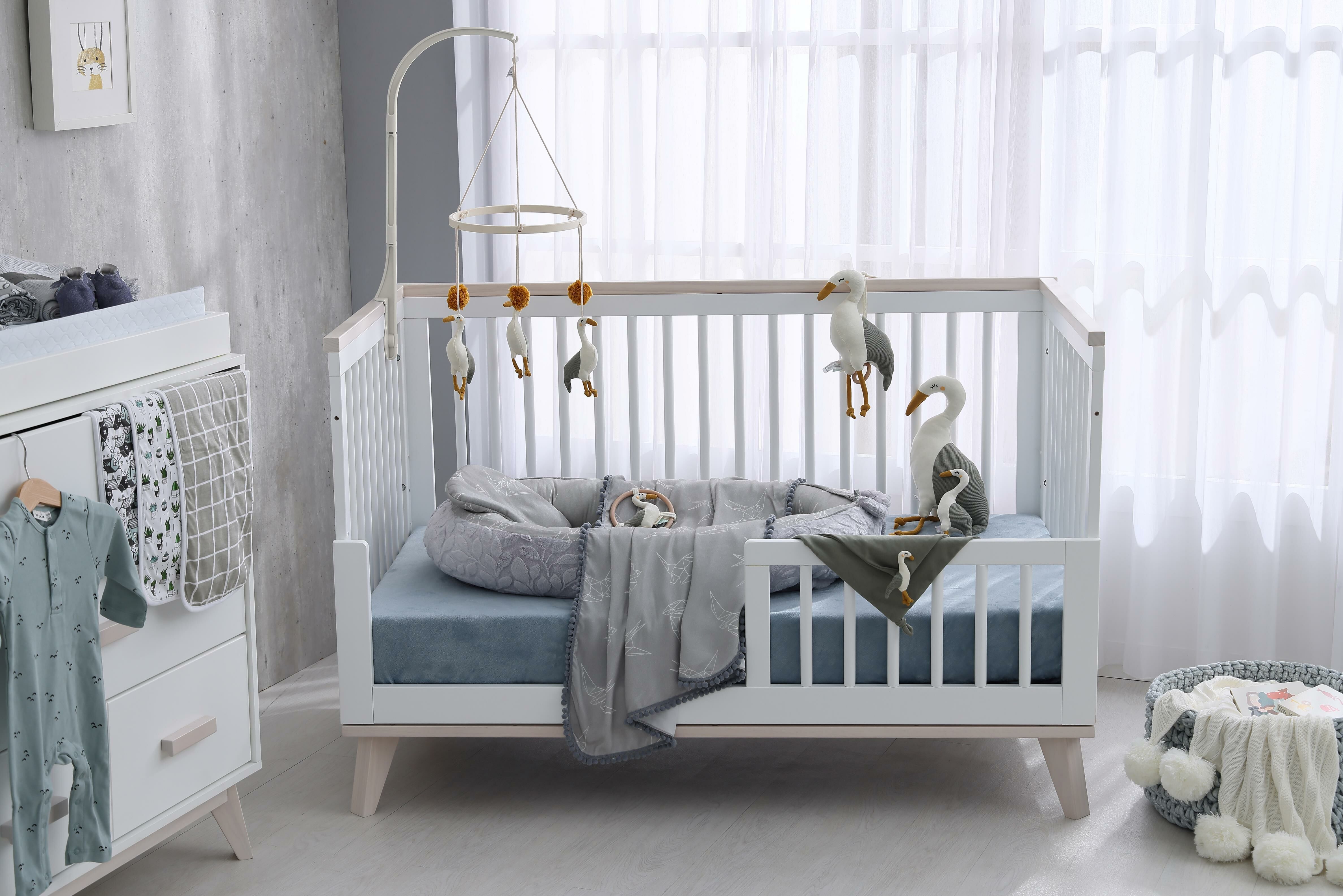 倫敦晨霧灰嬰兒房內的嬰兒床，上面擺著睡窩與各式安撫玩具