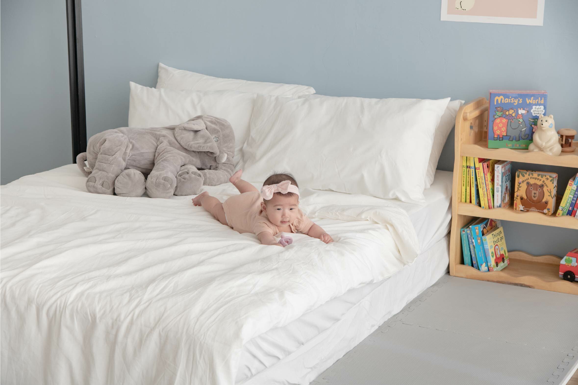 這是一張寶寶趴在床上、床邊有鋪地墊的照片