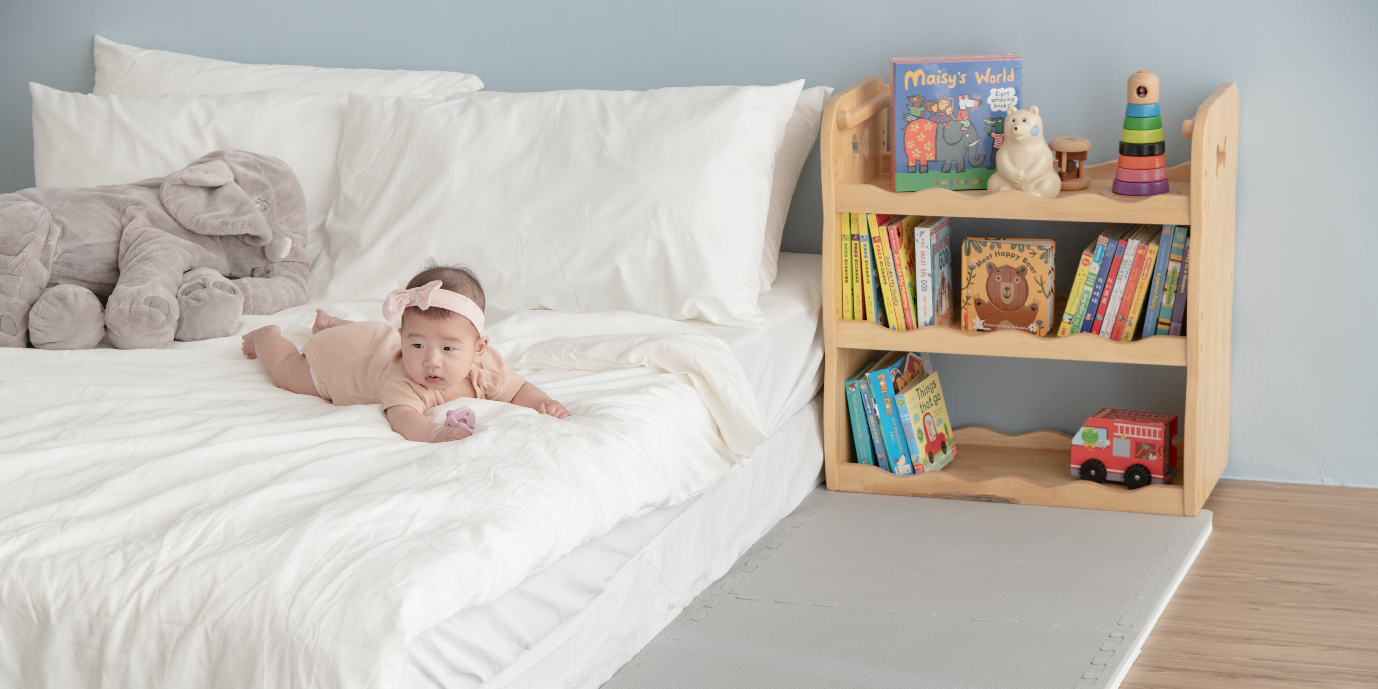 這是一張寶寶趴在床上、床邊有鋪地墊的照片