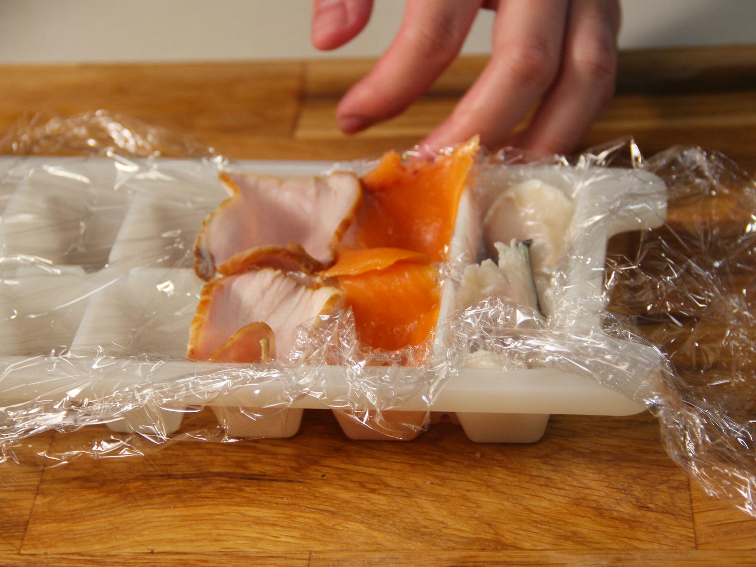取一個冰塊盒模具，撕保鮮膜放在模具上，放入鮭魚、火腿、鯖魚