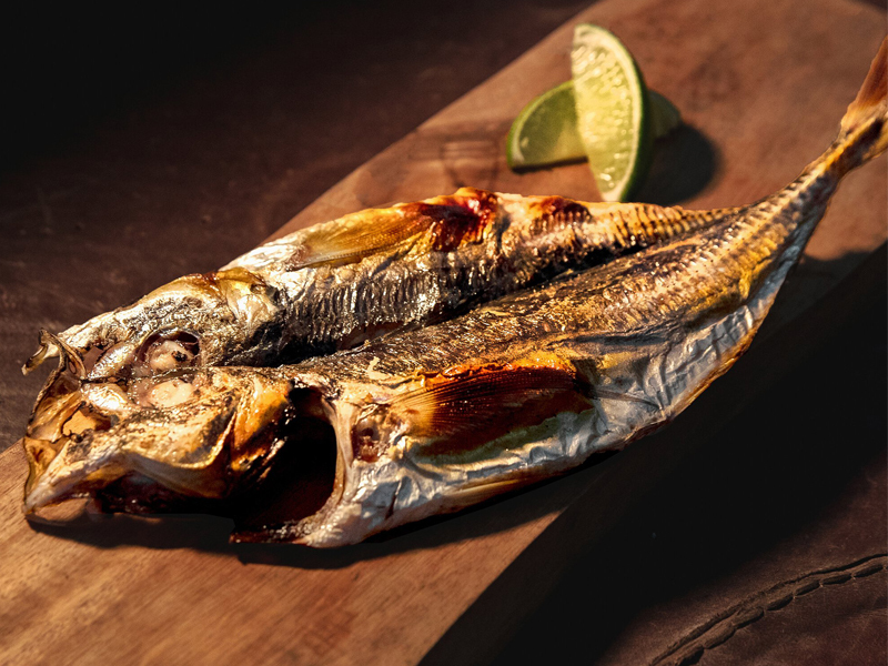 烤竹莢魚放在木板上，露出酥脆的魚皮，讓人想起居酒屋裡提供的美味佳餚。