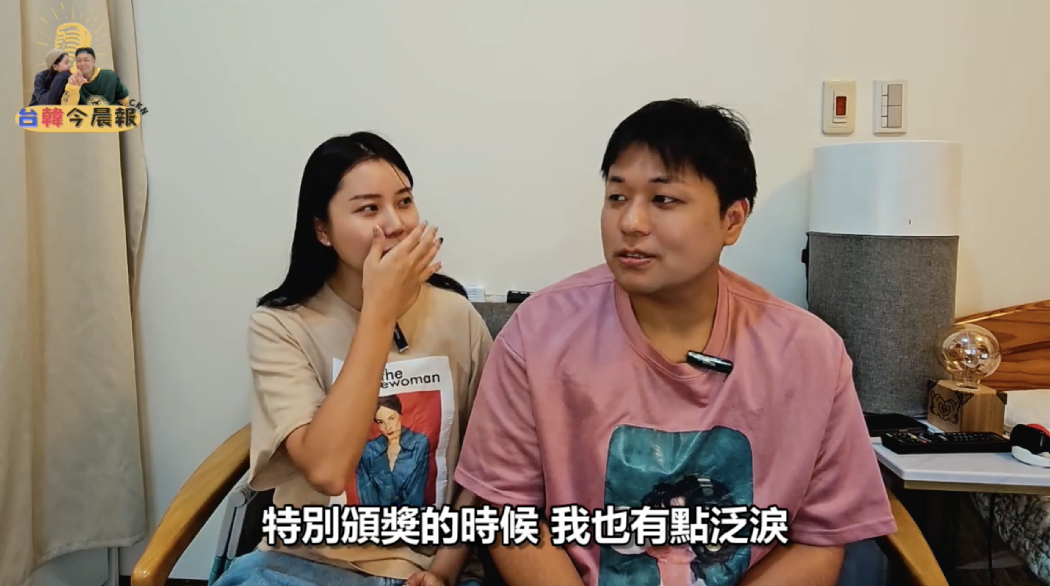 一名年輕女性和一名年輕男性坐在一起,女性用手掩嘴,看起來有些驚訝或感動。男性正在說話,畫面下方有字幕"特別頒獎的時候我也有點泛淚"。